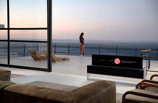 Téléviseur LG Signature OLED R installé sur une terrasse face à la mer, écran rangé dans son socle